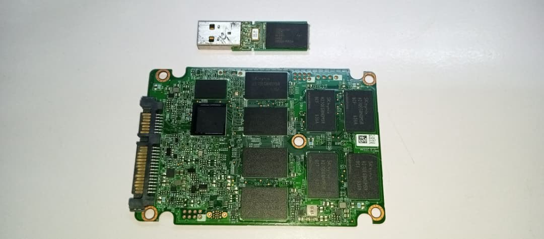 Placa de un SSD SATA de 2,5 pulgadas con sus chips de memoria NAND y, encima, una memoria USB sin carcasa